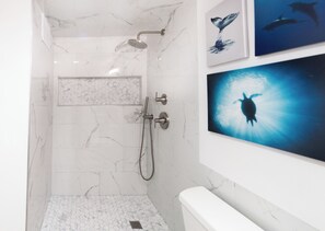 Une salle de bain moderne avec une douche, des toilettes et un lavabo. Trois tableaux encadrés ornent le mur.
