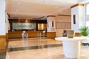 A hotel lobby with a reception desk, a large vase on a pedestal, and framed pictures on the wall.