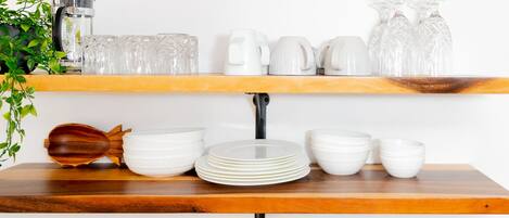 Une étagère de cuisine avec de la vaisselle en céramique blanche, une cuillère en bois et une machine à café.