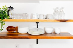 Une étagère de cuisine avec de la vaisselle en céramique blanche, une cuillère en bois et une machine à café.