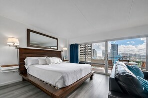 Une chambre d’hôtel avec un grand lit, un canapé, un balcon donnant sur la ville et une grande fenêtre.