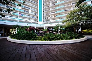 Un hôtel à plusieurs étages doté d’un atrium central, entouré d’une végétation luxuriante et d’une terrasse en bois.