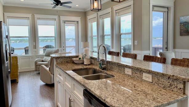A kitchen with granite countertops, a stainless steel sink, and a dishwasher. There are large windows offering a view of the water. - Flash Sale~Book Now~Tortuga Daybreak~Sleeps 8 (Gulf Shores)