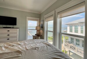 A bedroom with a bed, a dresser, a TV, and large windows with a view of a dock and water.