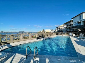 A swimming pool with a view of the ocean, a wooden deck, and a building with balconies.