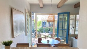 A kitchen with granite countertops, a dining area with a round table and chairs, and a view of a blue house through open doors. - Stunning 2bed/2bath Villa - Amazing Location+Views (La Quinta)