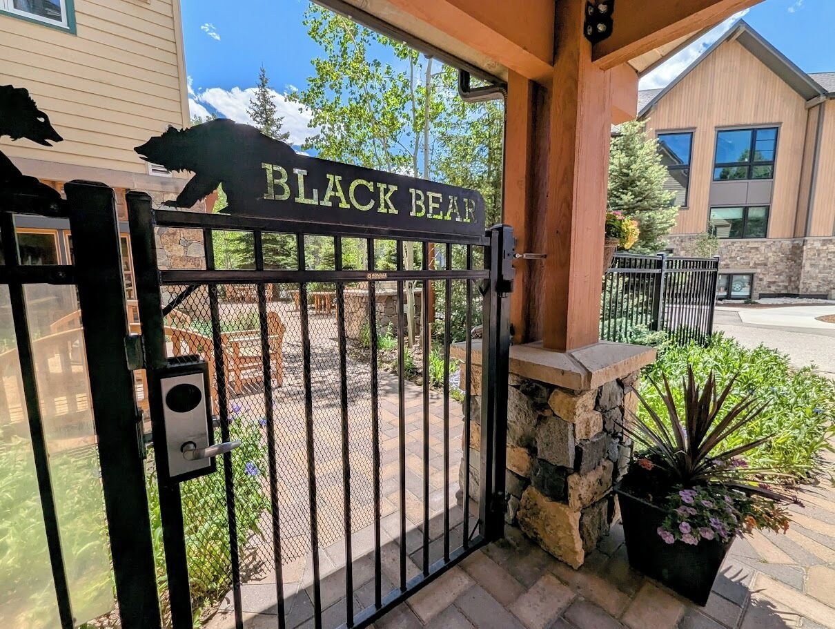 Una entrada protegida por un portón con un cartel que dice "BLACK BEAR" y un muro de piedra con una planta en maceta.