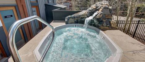A hot tub with a waterfall feature, surrounded by a stone wall and a metal railing.
