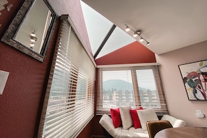 A corner room with a white sofa, red and white cushions, a painting on the wall, and a skylight above. - Lakeside 1497 (Keystone)