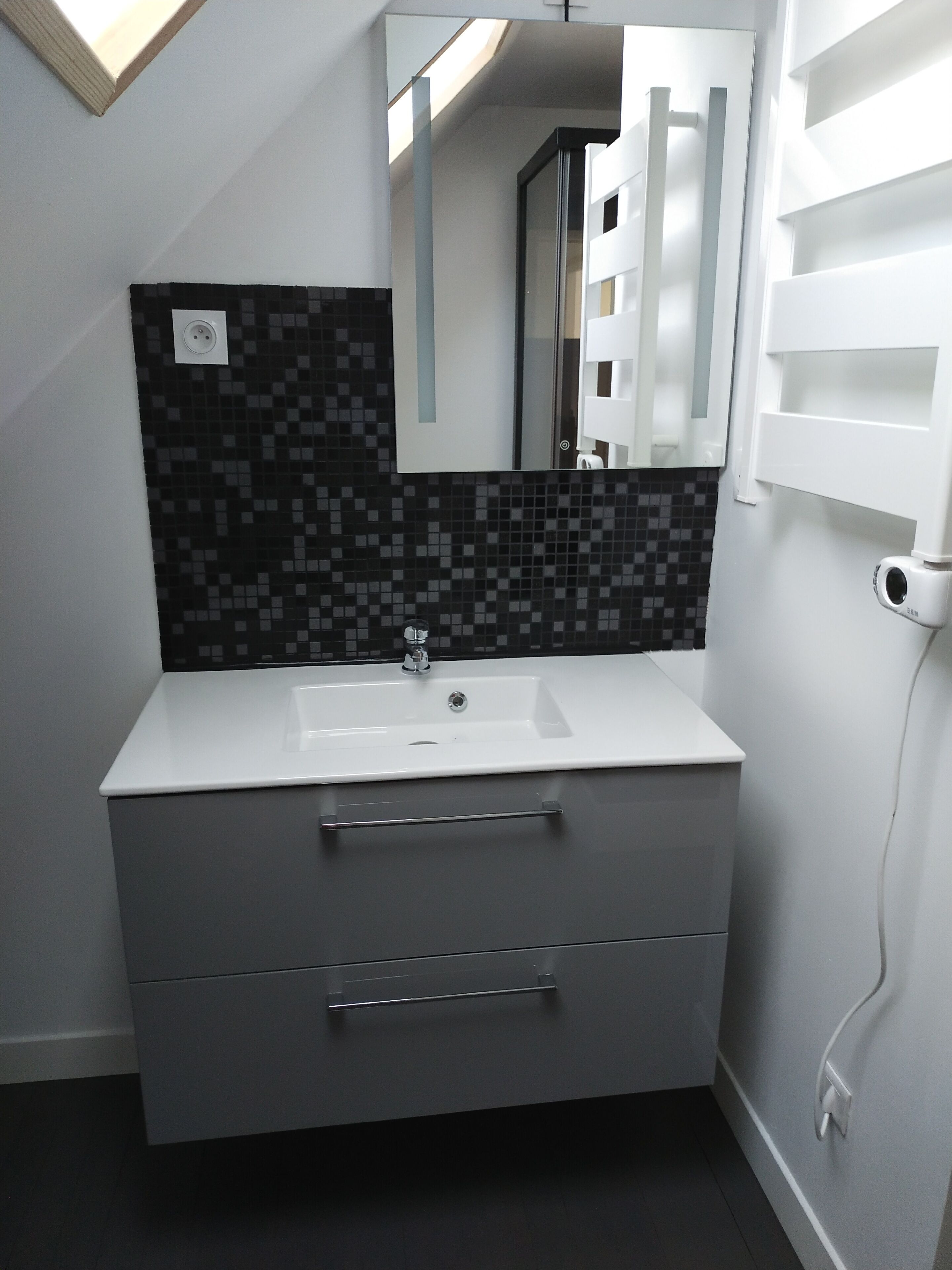 A modern bathroom with a white sink, a black and white tiled backsplash, a mirror, and a white towel rack.