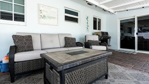 Ein überdachter Patio-Bereich mit einer Sofagarnitur, einem Couchtisch und einem Grill.
