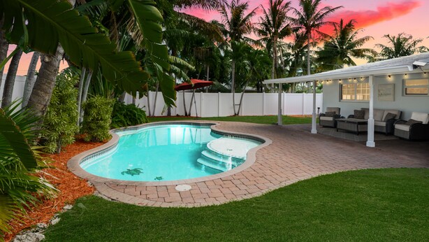 Ein Garten mit Swimmingpool, Palmen und einer überdachten Sitzgelegenheit.
