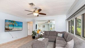 Ein Wohnzimmer mit einem großen Ecksofa, einem Deckenventilator und einem Gemälde mit Strandmotiv.