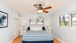 Ein Schlafzimmer mit Bett, Nachttischen, Deckenventilator, Fenster und Tür.