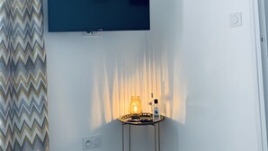 Et værelse med et fladskærms-tv monteret på væggen, et ur, et lille bord med en lampe og en gardin med et mønster.