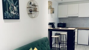 En moderne stue med en grøn sofa, et sofabord og et køkkenområde med hvide skabe og en sort bordplade.