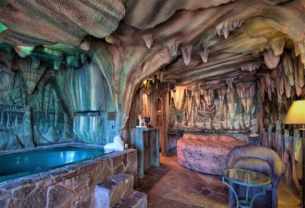A cave-themed room with a stone bathtub, a cushioned seating area, and a glass table.