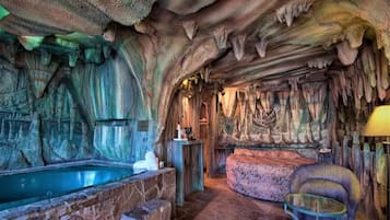 A cave-themed room with a stone bathtub, a cushioned seating area, and a glass table.