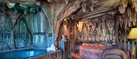 A cave-themed room with a stone bathtub, a cushioned seating area, and a glass table.