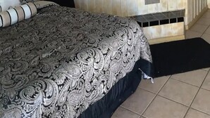 A room with a large bed, a black and white patterned bedspread, a black and white tiled bathroom, and a black bathtub.
