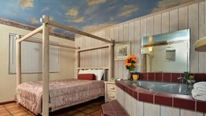 A room with a bed, a bathroom with a sink and mirror, and a ceiling with a painted sky design.