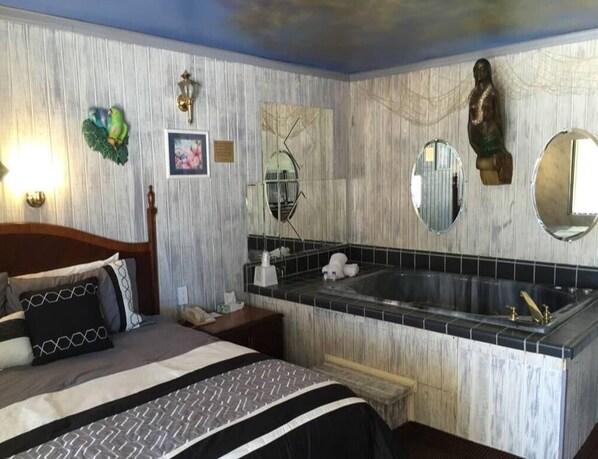 A hotel room with a bed, a large bathtub, and a wooden headboard.