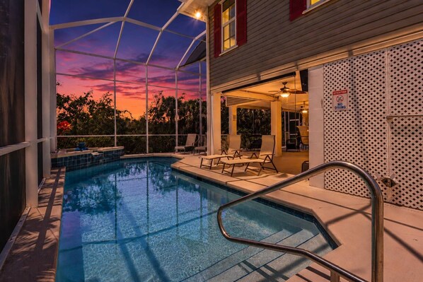 A swimming pool with a view of a sunset, outdoor seating, and a covered patio area. - 27090 Belle Rio Dr (Bonita Springs)