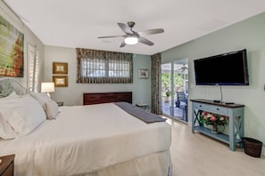 A hotel room with a bed, a ceiling fan, a television, and a view of the outdoors. - 27090 Belle Rio Dr (Bonita Springs)