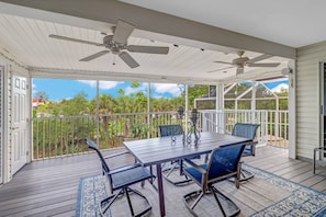 A covered patio with a table and chairs, ceiling fans, and a view of greenery.