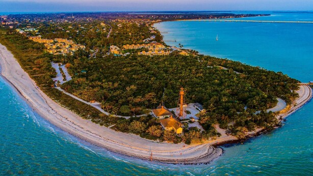 An aerial view of a coastal area with a lighthouse, beach, and residential buildings. - 27090 Belle Rio Dr (Bonita Springs)