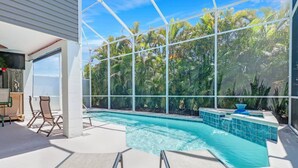 A modern indoor pool with clear blue water, surrounded by large windows offering views of lush tropical vegetation. - 27090 Belle Rio Dr (Bonita Springs)