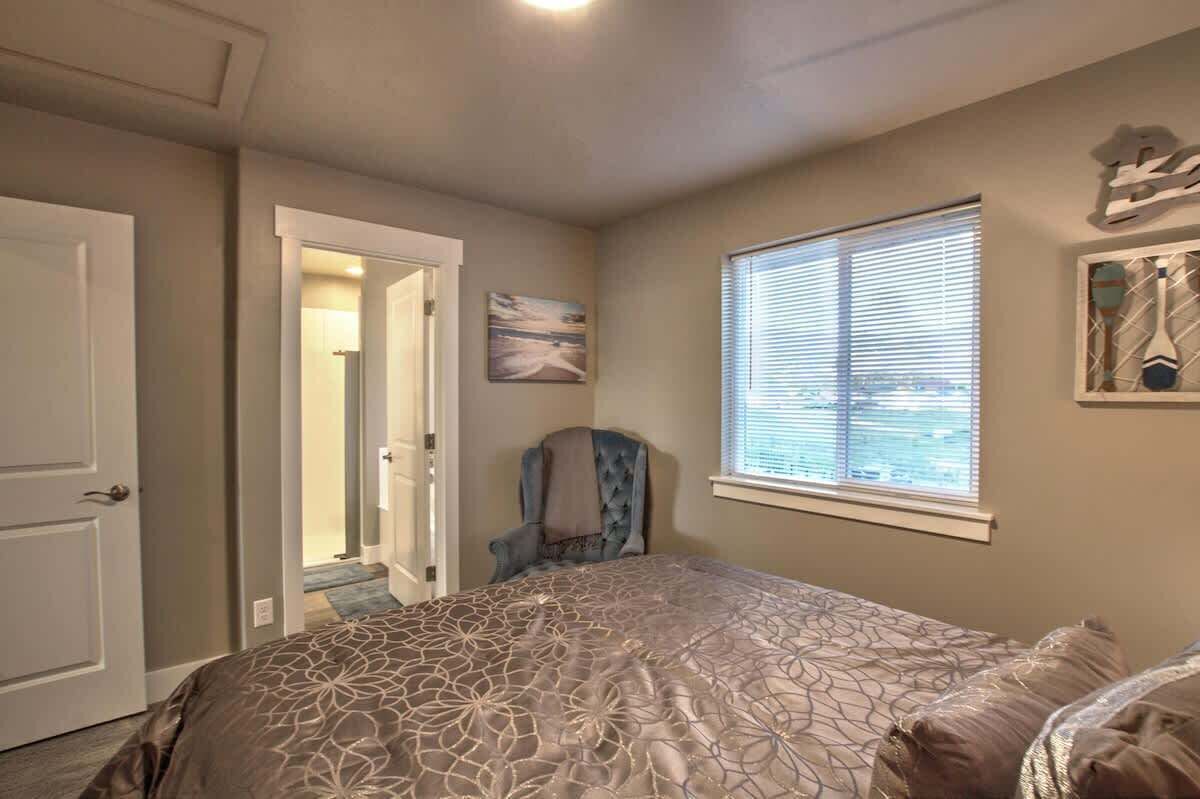 A bedroom with a bed, a chair, a window with blinds, and a door.
