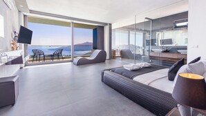 Ein modernes Hotelzimmer mit großem Balkon, einer Sitzecke, einem Fernseher und einem Badezimmer mit Glasdusche.