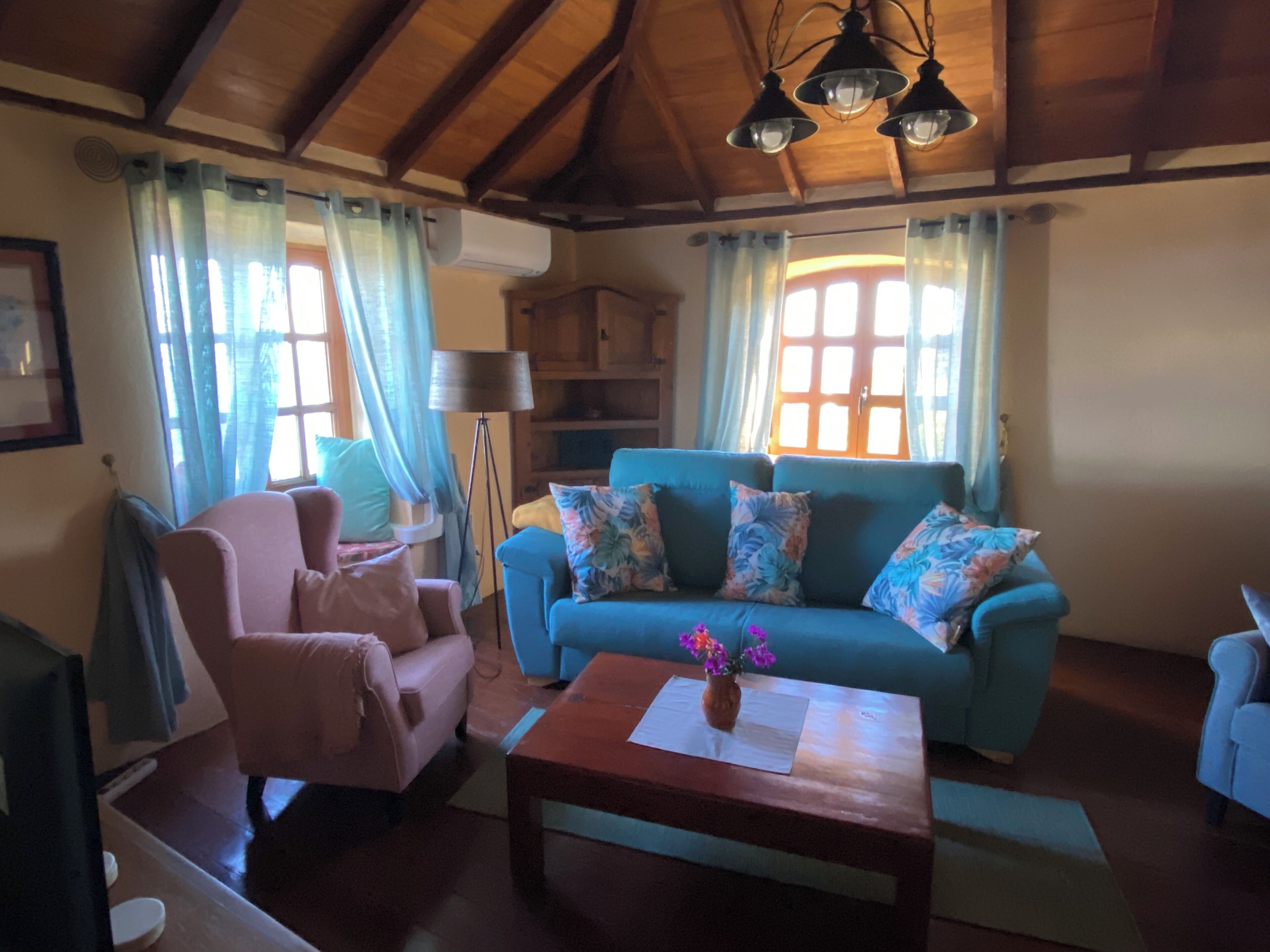A cozy living room with a blue sofa, a pink armchair, and a wooden coffee table. There is a floor lamp and a window with curtains.