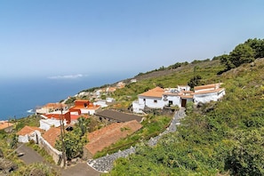 Uma vila costeira com edifícios brancos e telhados vermelhos, rodeada por vegetação e com vista para o mar.