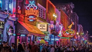 Une rue animée, illuminée par des enseignes au néon, dont les panneaux « Second Fiddle » et « Layla's Welcome to Nashville ».