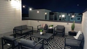 A rooftop patio with outdoor furniture, string lights, and potted plants.