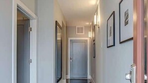 A hallway with a polished floor, framed artwork on the walls, and a door at the end.