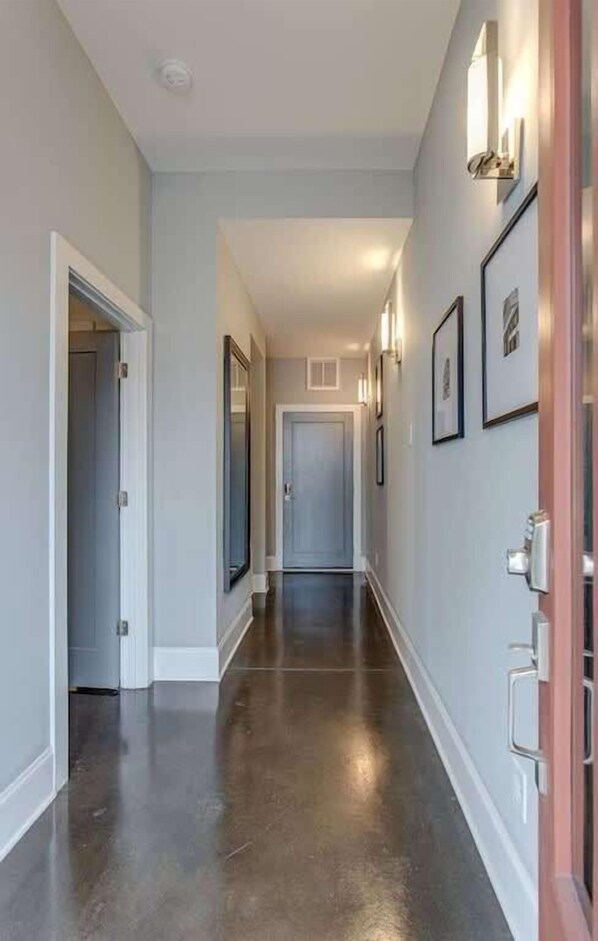 A hallway with a polished floor, framed artwork on the walls, and a door at the end.