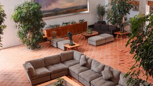 A spacious living area with a sectional sofa, a coffee table, and a TV. There are multiple potted plants and hanging decorations. - El Diezmo Hotel (San José Iturbide)