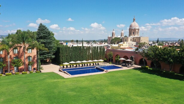 A courtyard with a swimming pool, a large building with a dome, and a clear blue sky. - El Diezmo Hotel (San José Iturbide)
