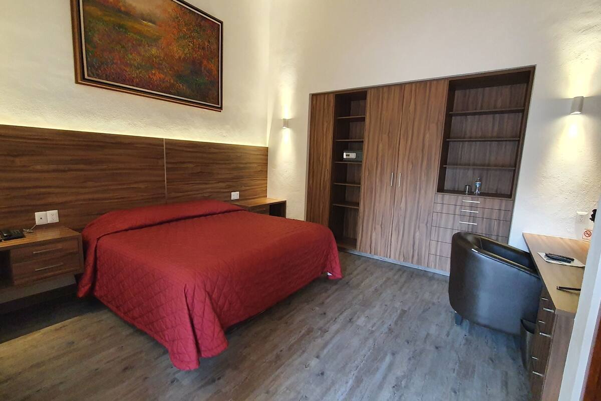 Ein Schlafzimmer mit Bett, Schreibtisch, Stuhl, Kleiderschrank und einem Bild an der Wand.
