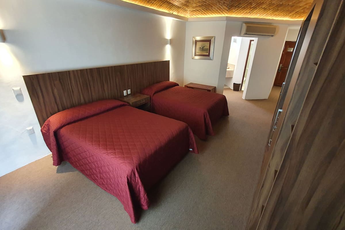 Ein Hotelzimmer mit zwei Betten, einem Holzkopfstück, einem kleinen Nachttisch und einer wandmontierten Klimaanlage.