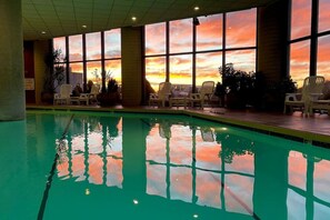 A swimming pool with clear water reflecting the sunset sky, surrounded by lounge chairs and large windows. - 2019 Sugartop Mountain Condo- Views, Pool, Hot tub (Sugar Mountain)
