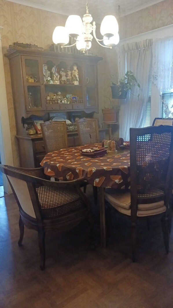 Une salle à manger avec une table en bois, quatre chaises, un lustre et un buffet orné de statuettes.