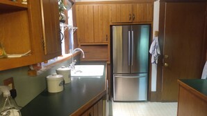 A kitchen with wooden cabinets, a stainless steel refrigerator, a sink, and a countertop with a bottle of window cleaner. - GRANDMA'S COTTAGE  (Monticello)