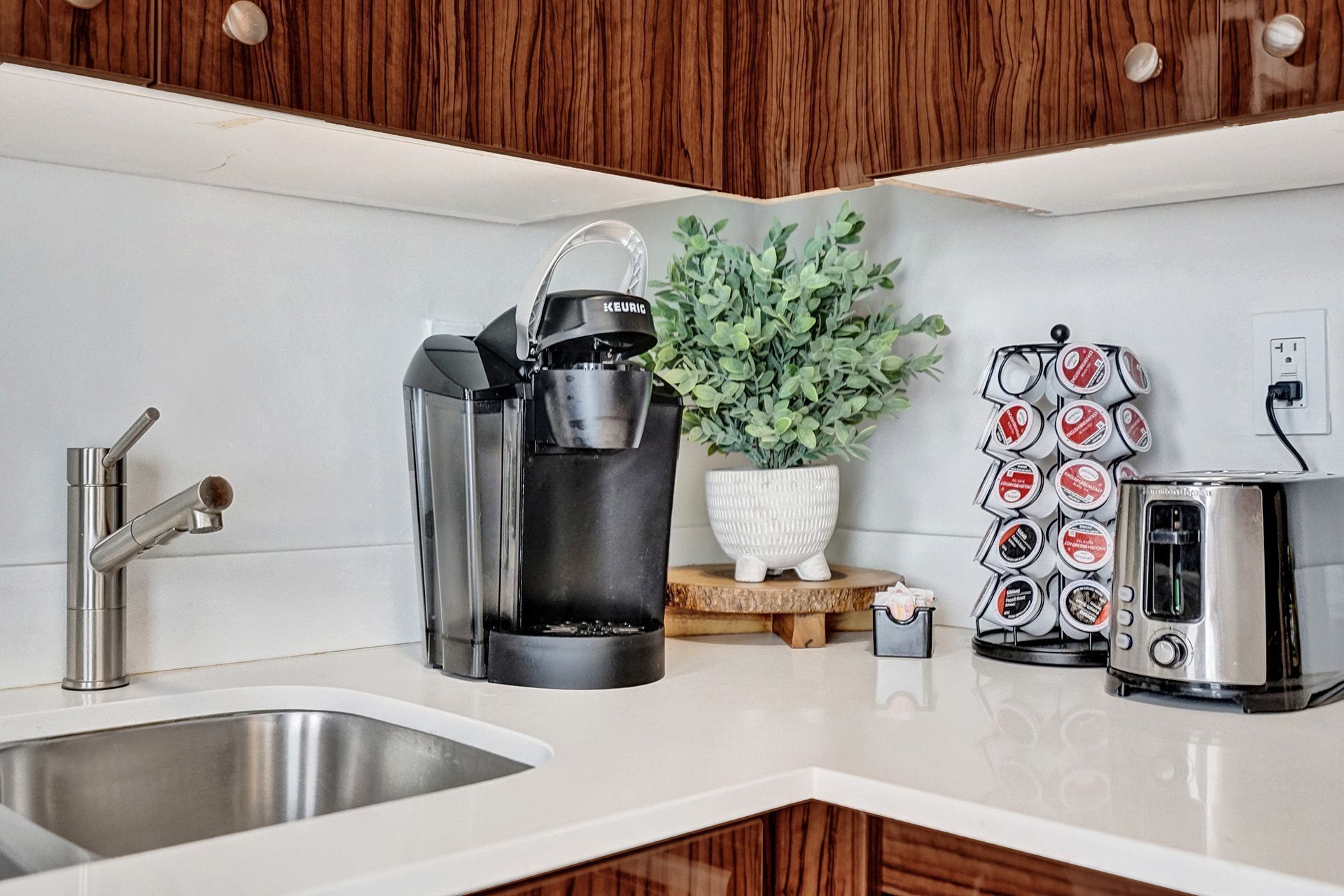 A kitchen with a coffee maker, a toaster, a sink, and a potted plant.