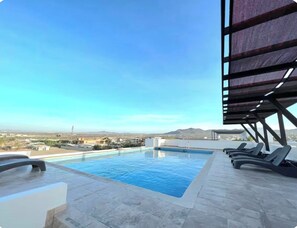 Una piscina en la azotea con sillas de descanso y vistas al paisaje.