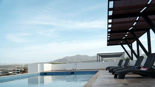 Una piscina infinita en la azotea con sillones de descanso y una pérgola, con vistas a un paisaje montañoso.