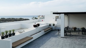 Terraza en la azotea con vistas al mar, que cuenta con un área de descanso con cojines y plantas en macetas.